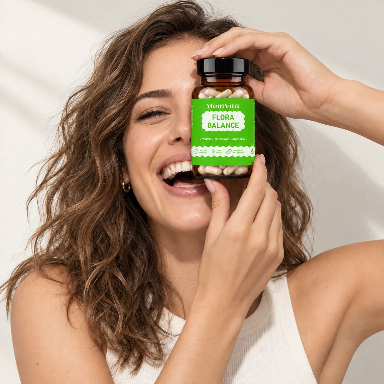 Lachende Frau hält ein Glas mit MeinVita Flora Balance vor ihr Gesicht